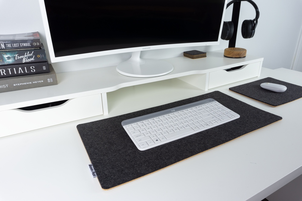Black wool felt and cork desk mat from an angle. White keyboard on desk mat, next to matching black wool mouse pad