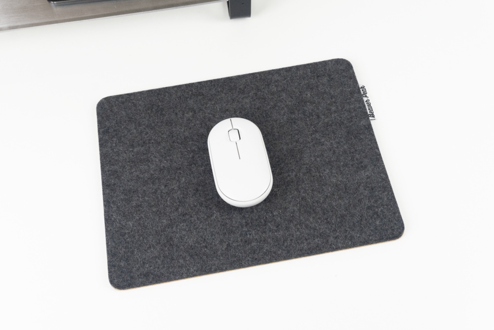 Black merino wool mouse pad with white mouse in middle, sitting on desk.