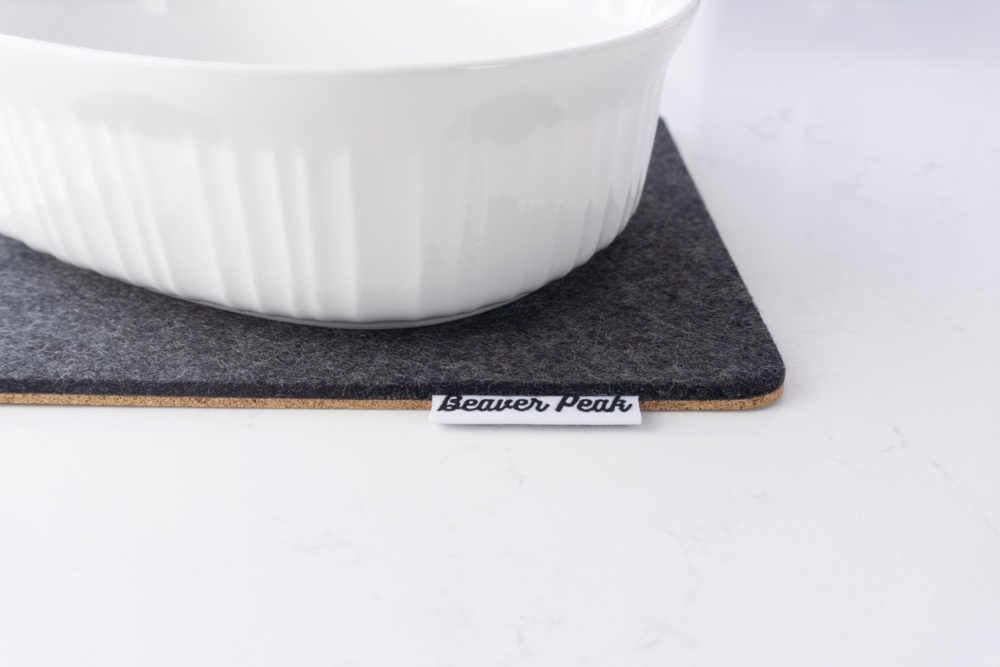 Black wool felt trivet with white ceramic pot on top.