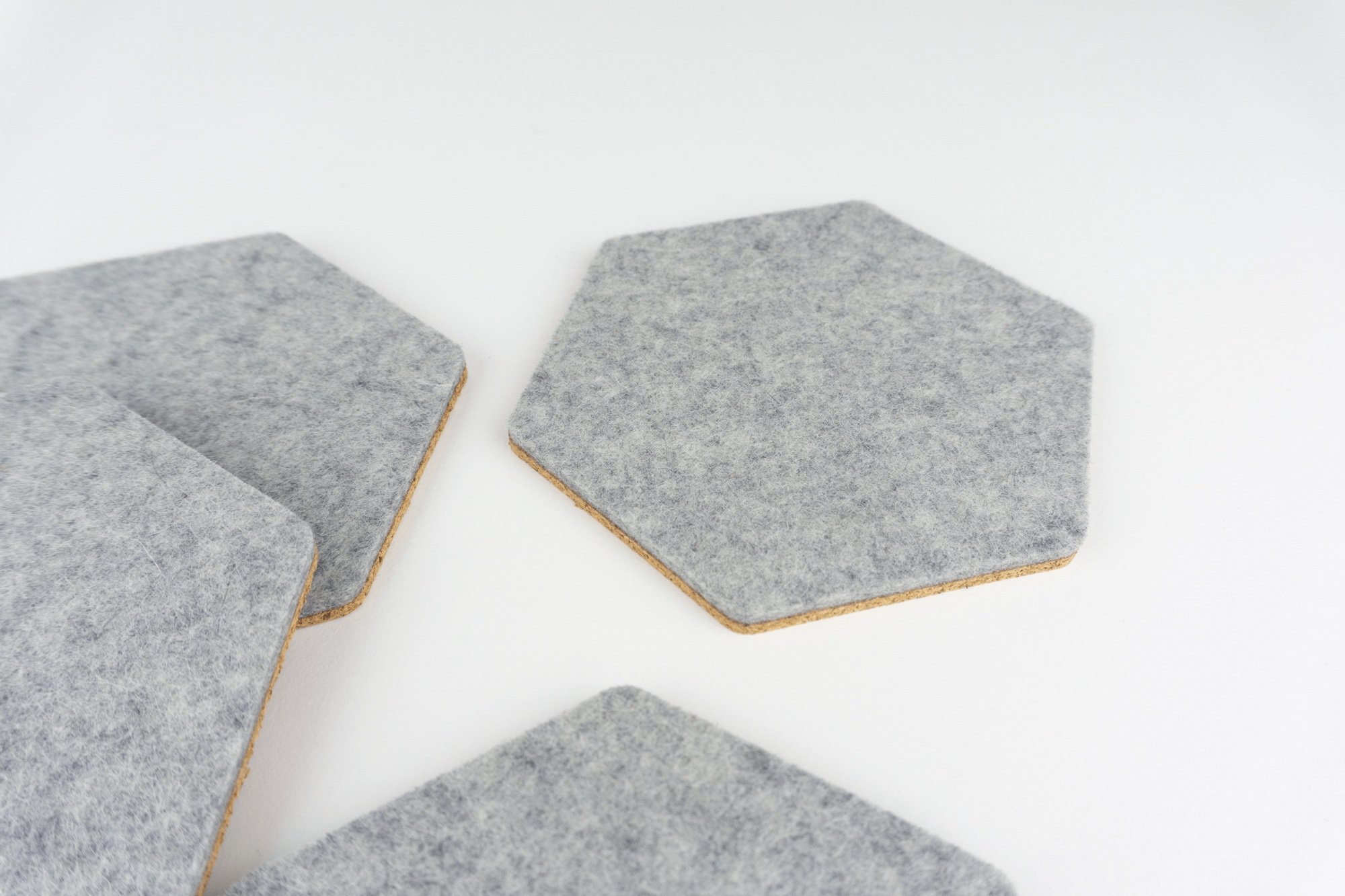 A close up of 4 grey wool felt hexagon coasters shown on a white desk spread out.