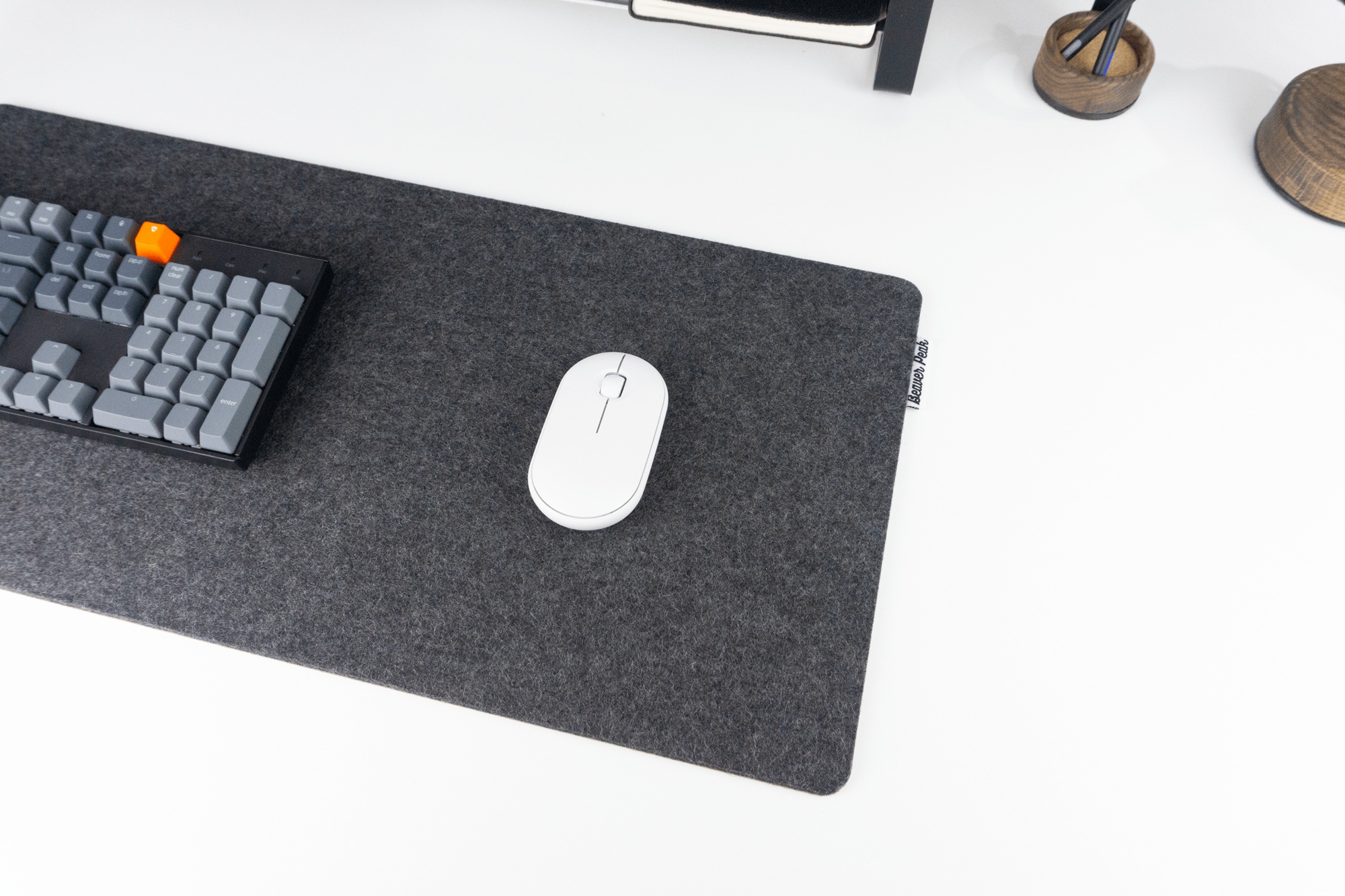 Black wool and cork desk pad with white mouse and mechanical keyboard on top. The wool desk pad is on a standing desk and has a BeaverPeak logo tag protruding from the right side of the mat.