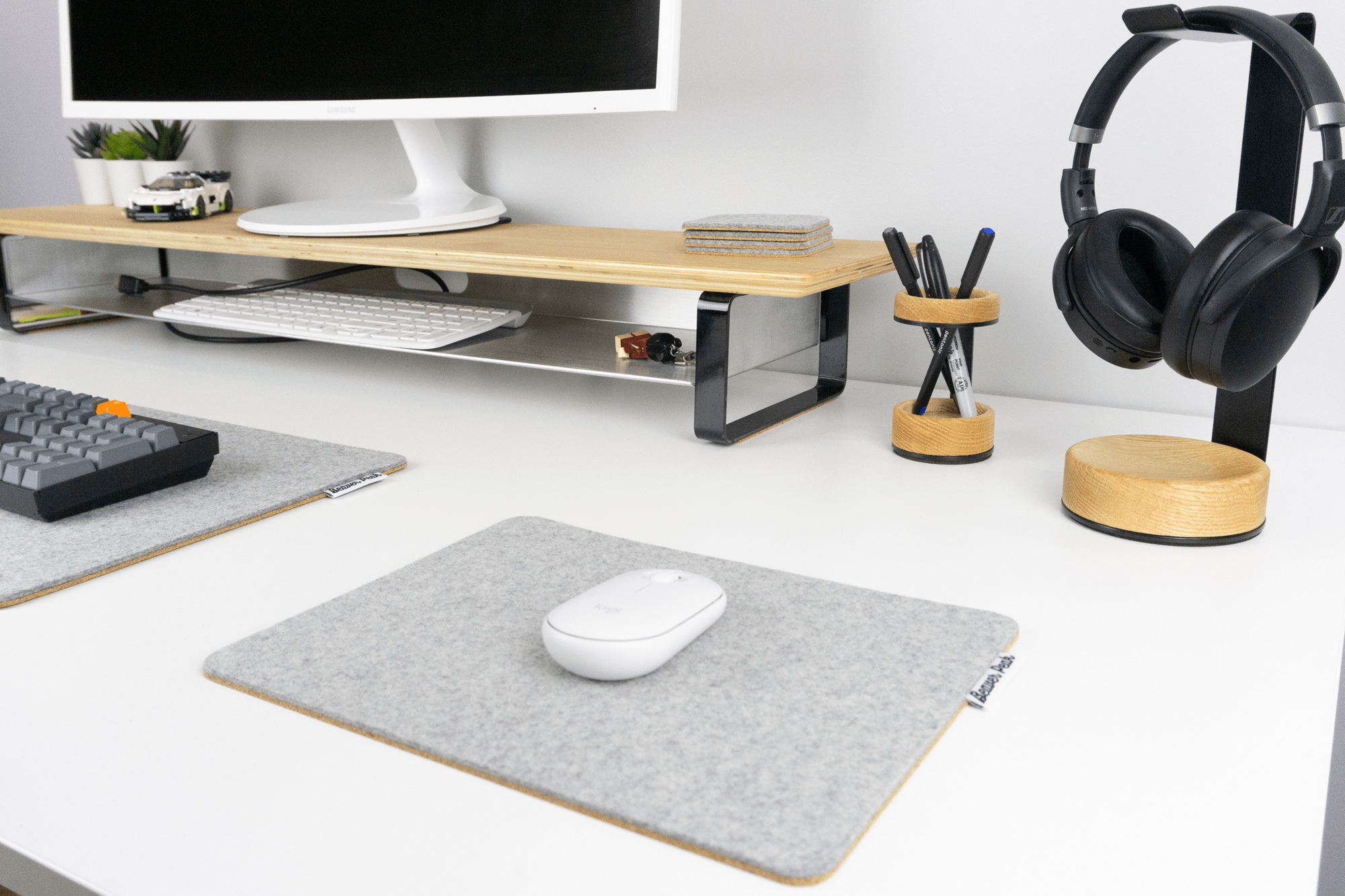 Closeup of our grey mouse pad next to grey desk mat and oak headphone stand. Wood desk shelf in background. The entire desk setup contains desk accessories from BeaverPeak.