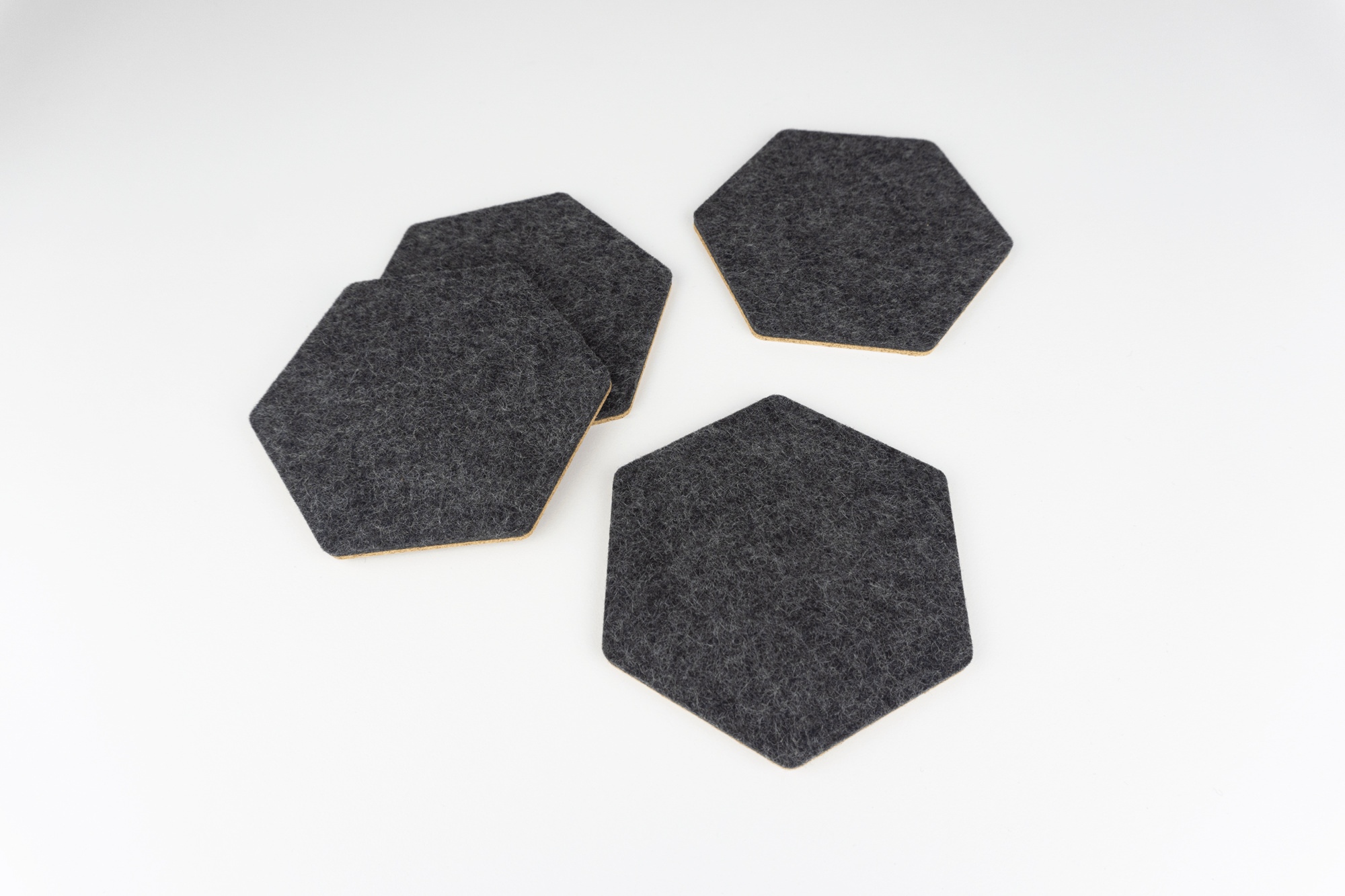A set of 4 black wool and cork hexagon coasters shown on a white desk spread out.