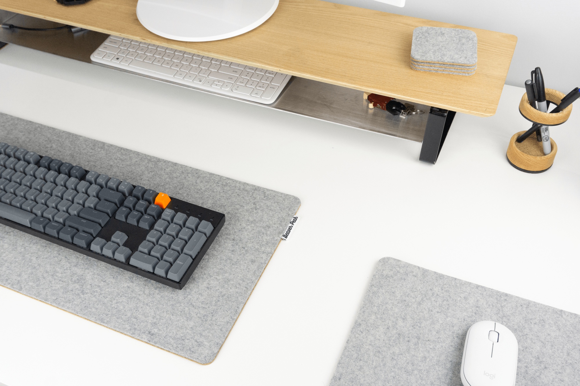 Grey wool mousepad next to matching grey desk mat. Desk also includes pen stand and desk shelf