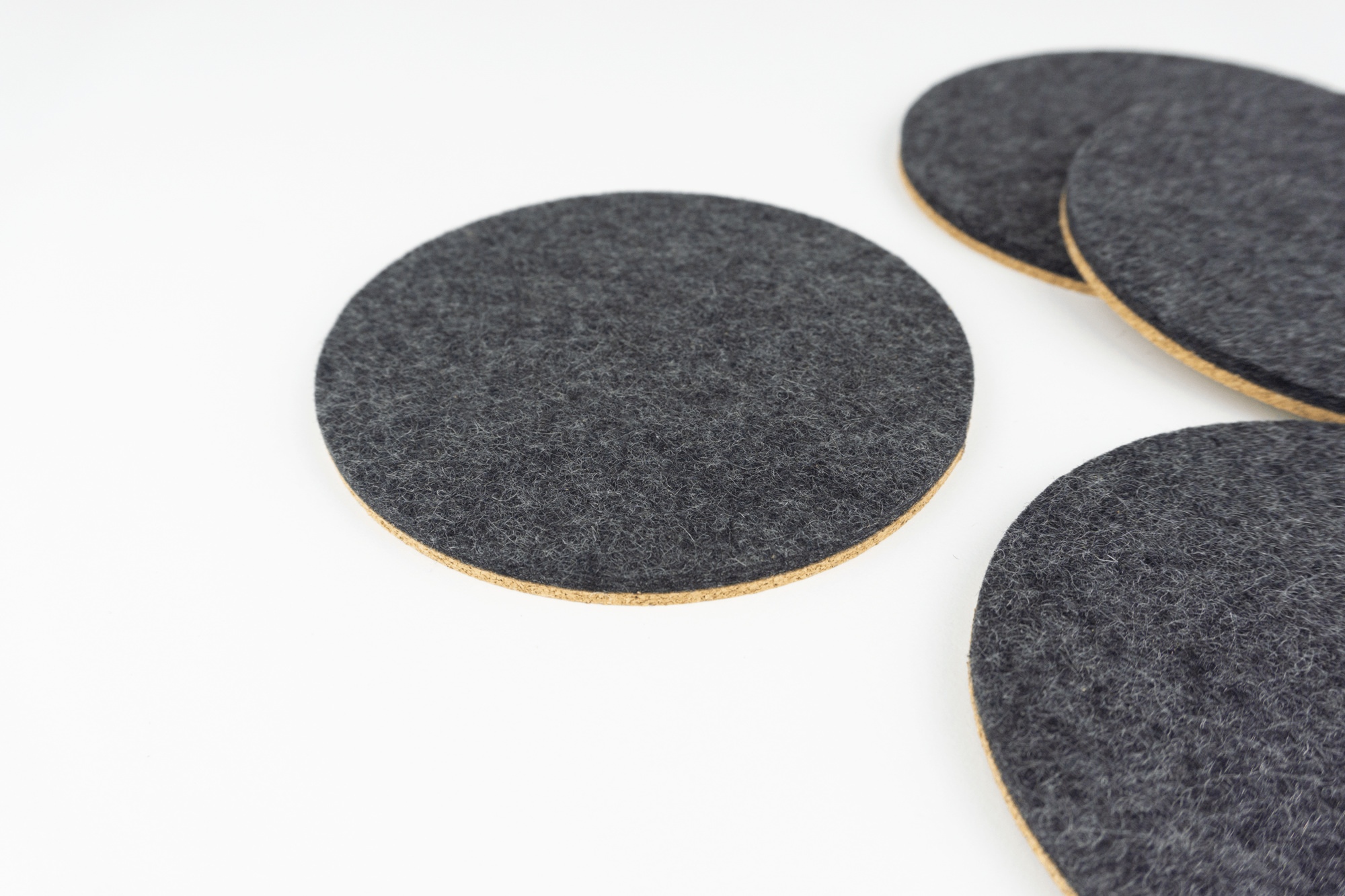 Our black wool and cork circular coasters shown spread out on a white coffee table.