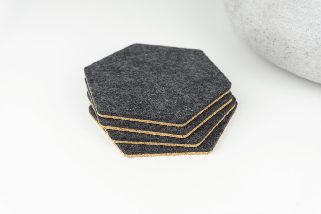 4 of our hexagon coasters on a coffee table. Our coasters are made with black merino wool and cork.