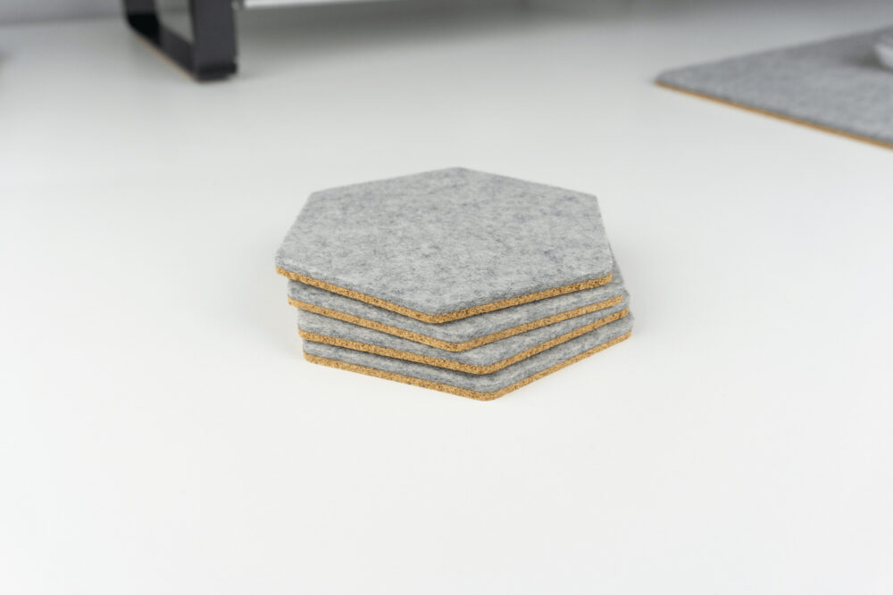 A stack of 4 hexagon coasters on a desk made with grey merino wool cork.
