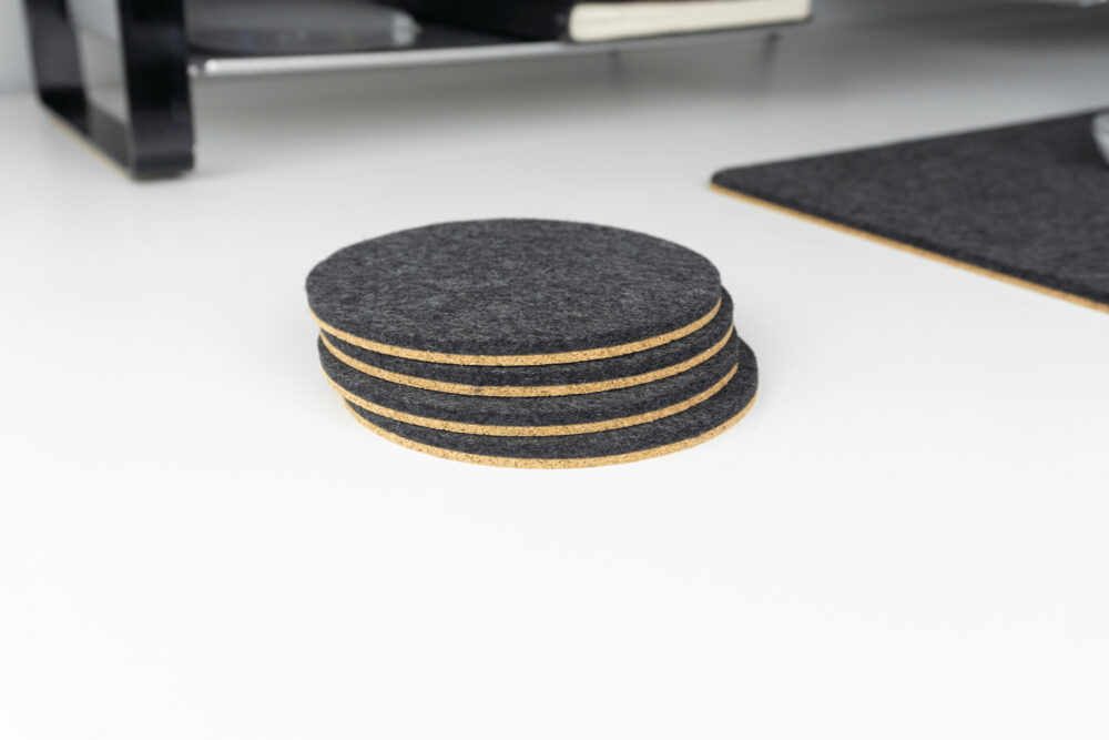 A set of our black circle coasters shown on a white desk top next to a matching black wool desk pad.