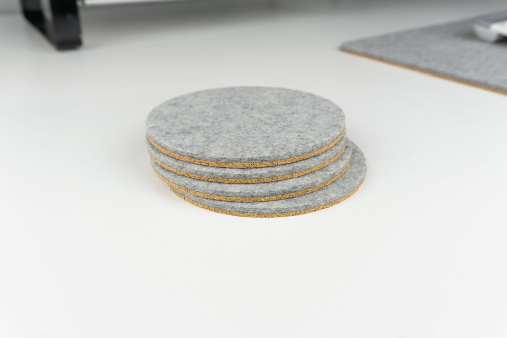 A set of our circle desk coasters shown on a white desk next to a matching grey wool desk mat.