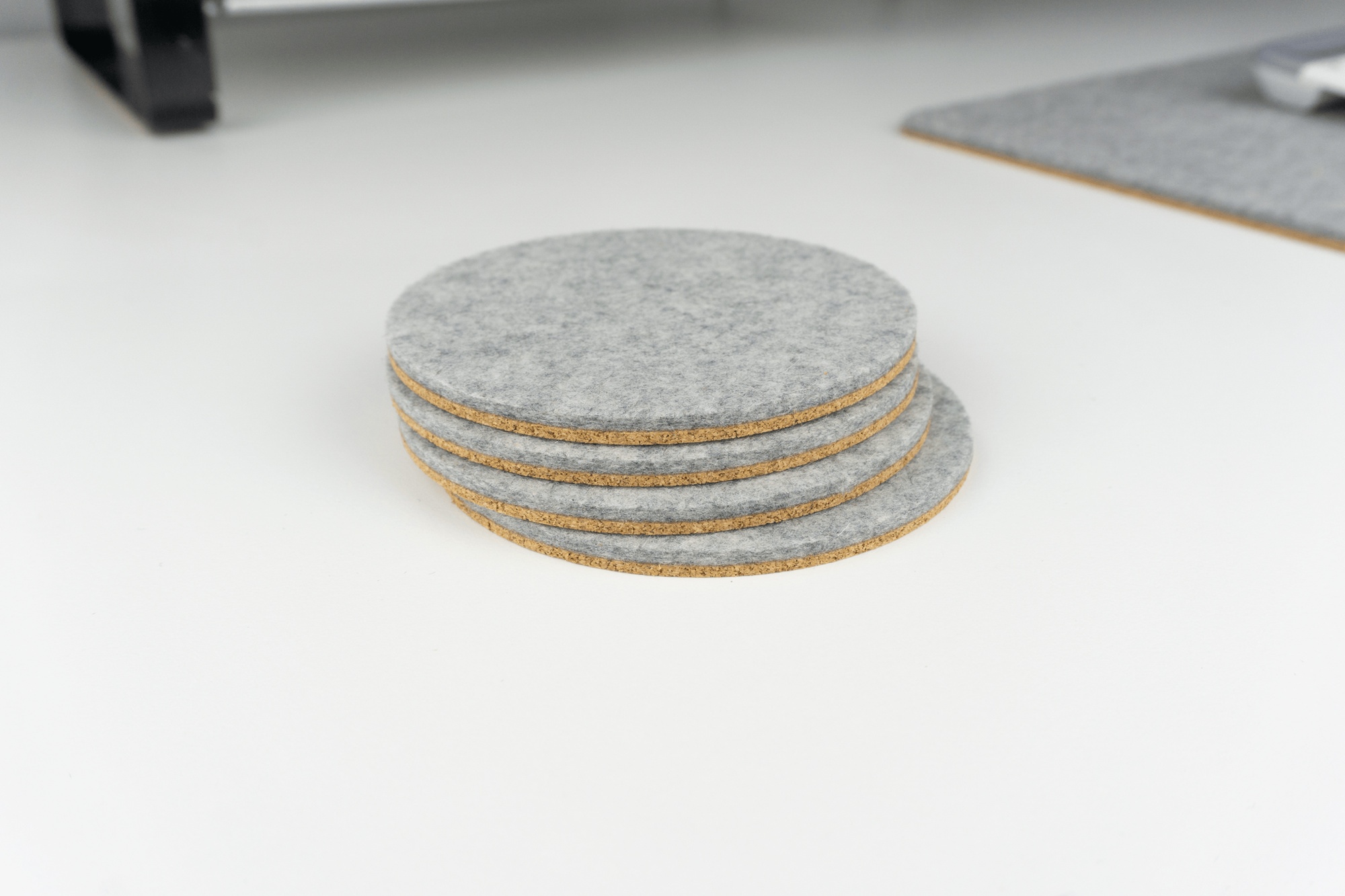 A set of our circle desk coasters shown on a white desk next to a matching grey wool desk mat.