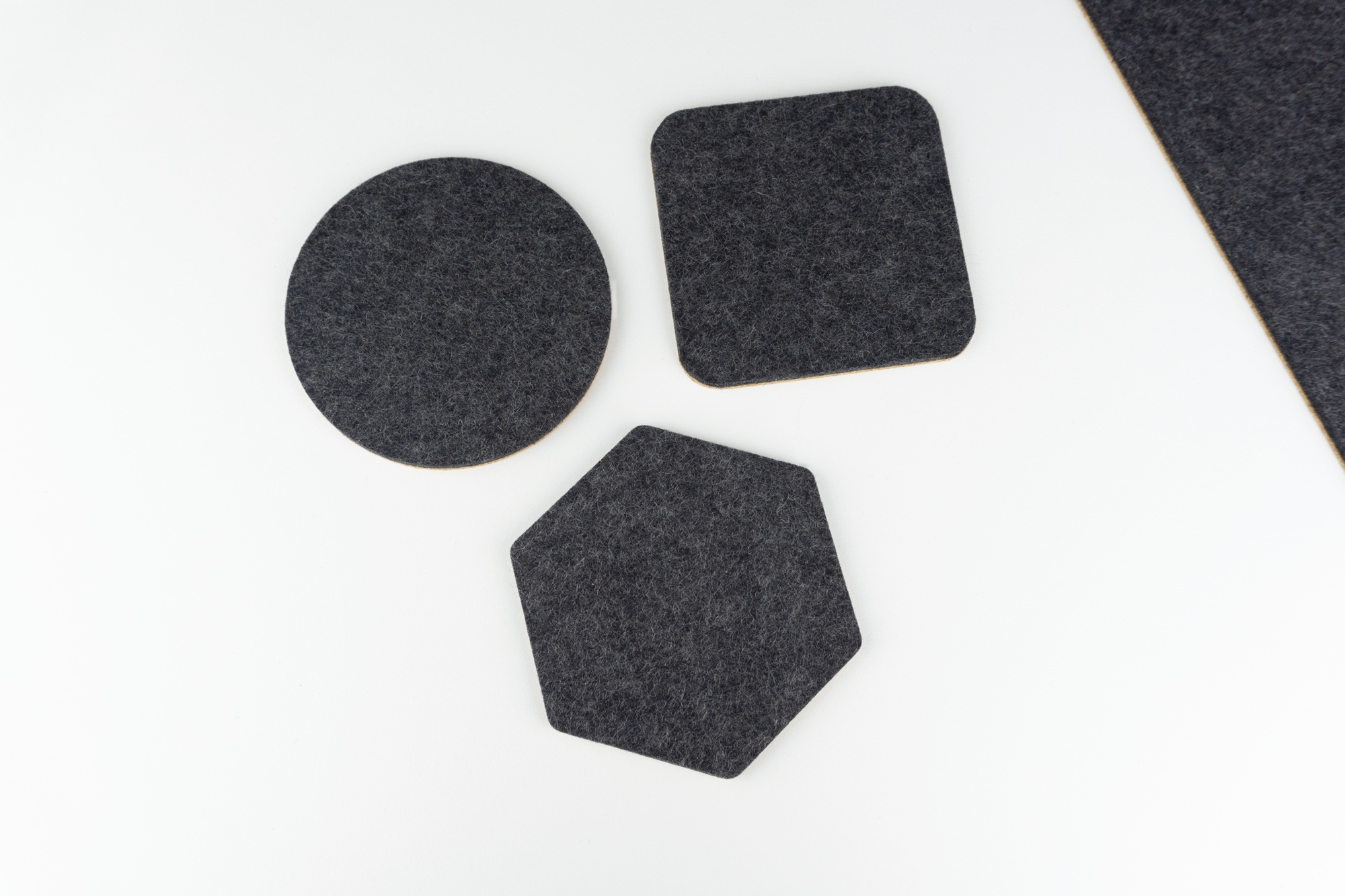 All of our coaster types on a white desk top. Our square, circle and hexagon coasters are shown in black wool felt.